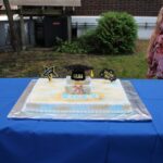 A woman is standing in front of a graduation cake.