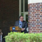 A man standing at a podium in front of a brick building.