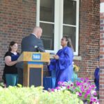 A woman is giving a speech at a podium in front of a brick building.