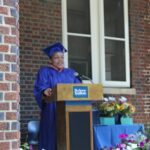 A woman in a blue graduation gown standing at a podium.