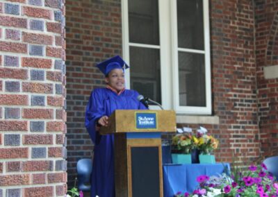 A woman in a blue graduation gown standing at a podium.