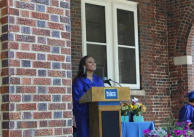 A woman speaking at a podium in front of a brick wall.