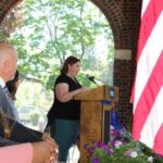 A woman speaks at a podium in front of an american flag.