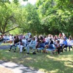 A large group of people sitting on chairs in a park.