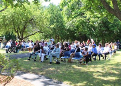 A large group of people sitting on chairs in a park.