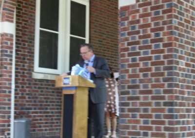 A man standing at a podium in front of a brick building.