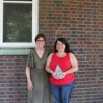 Two women standing in front of a brick building.
