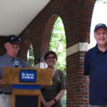 Three people standing at a podium in front of a brick wall.