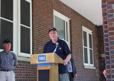 Two men standing at a podium in front of a brick building.