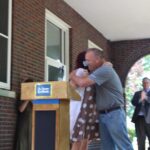 Two people hugging at a podium in front of a building.