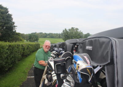 A man standing next to a golf cart full of golf clubs.