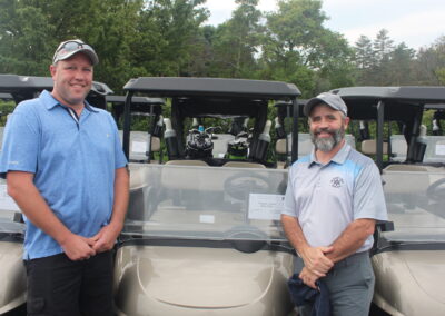 Two men standing next to a golf cart.