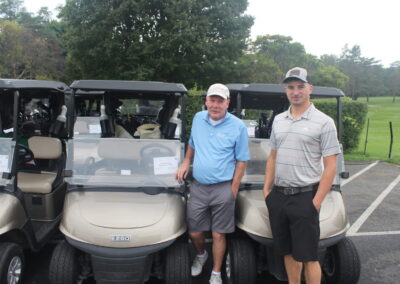 Two men standing next to golf carts in a parking lot.