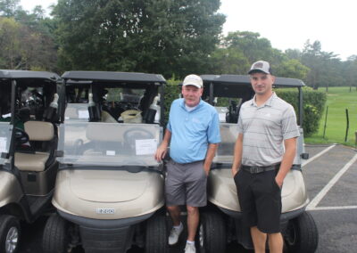 Two men standing next to golf carts in a parking lot.