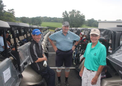 Three men standing next to golf carts.