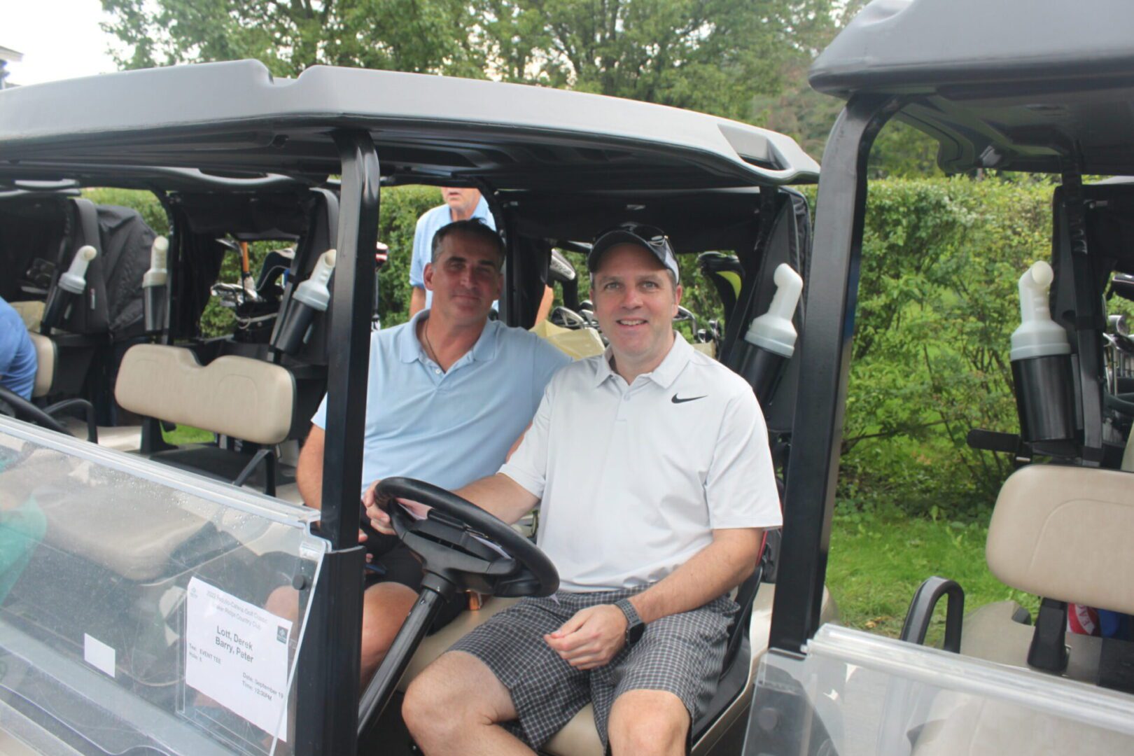 Two men sitting in the back of a golf cart.