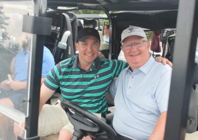 Two men sitting in the driver's seat of a golf cart.