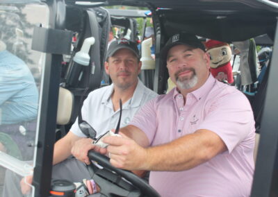 Two men sitting in the driver's seat of a golf cart.