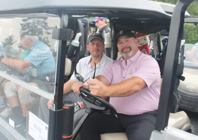 Two men sitting in the driver's seat of a golf cart.