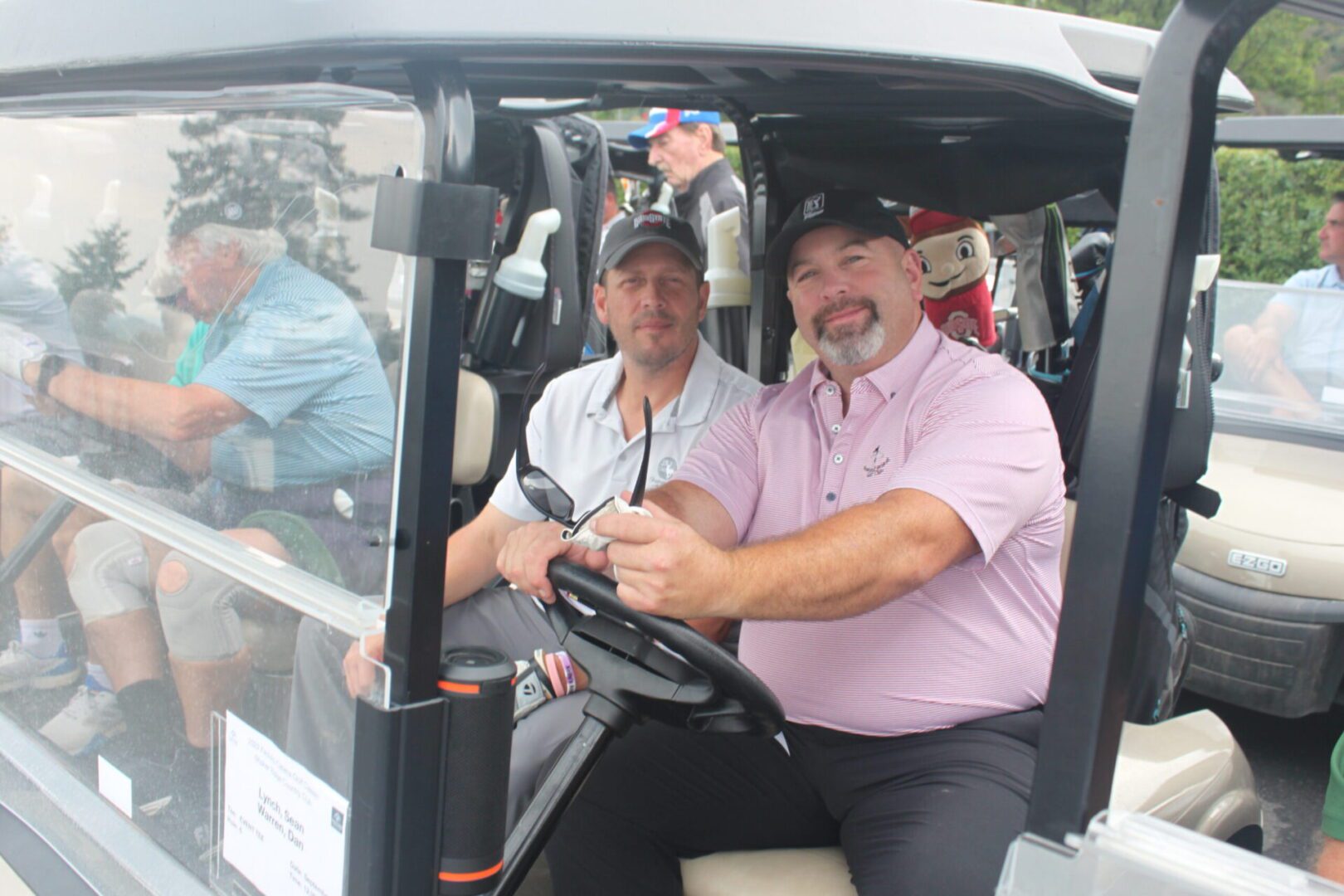 Two men sitting in the driver's seat of a golf cart.