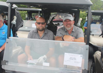 Two men sitting in a golf cart at a tournament.