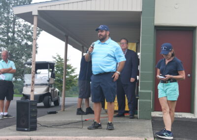 A man is standing in front of a building with a microphone.