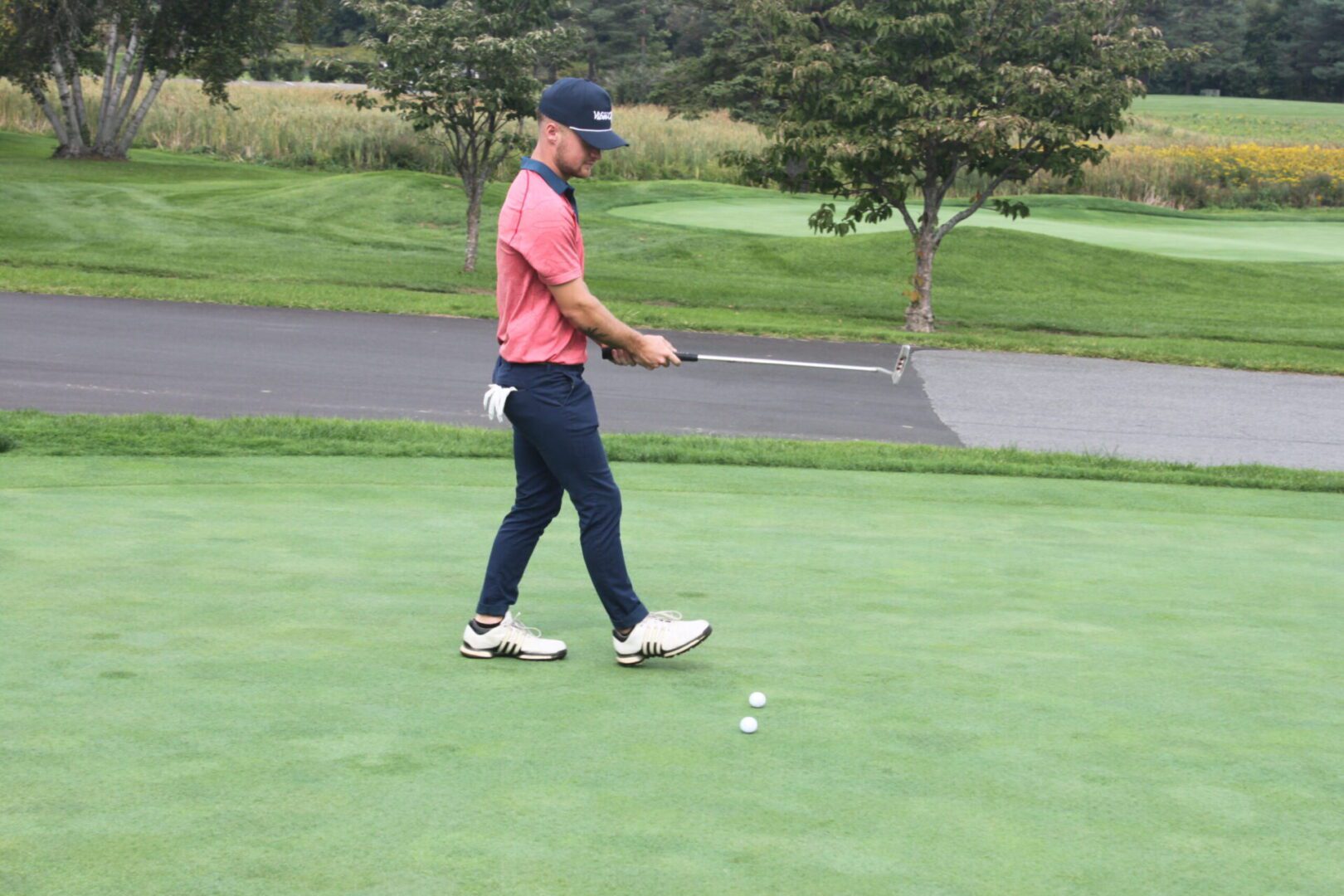 A man in a pink shirt is putting on a golf course.