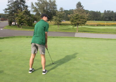 A man in a green shirt is putting a golf ball.