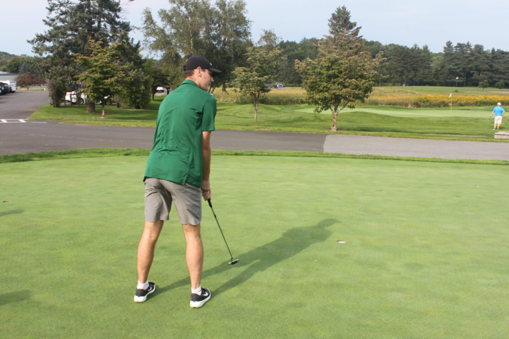 A man in a green shirt is putting a golf ball.