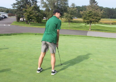 A man in a green shirt is putting a golf ball.