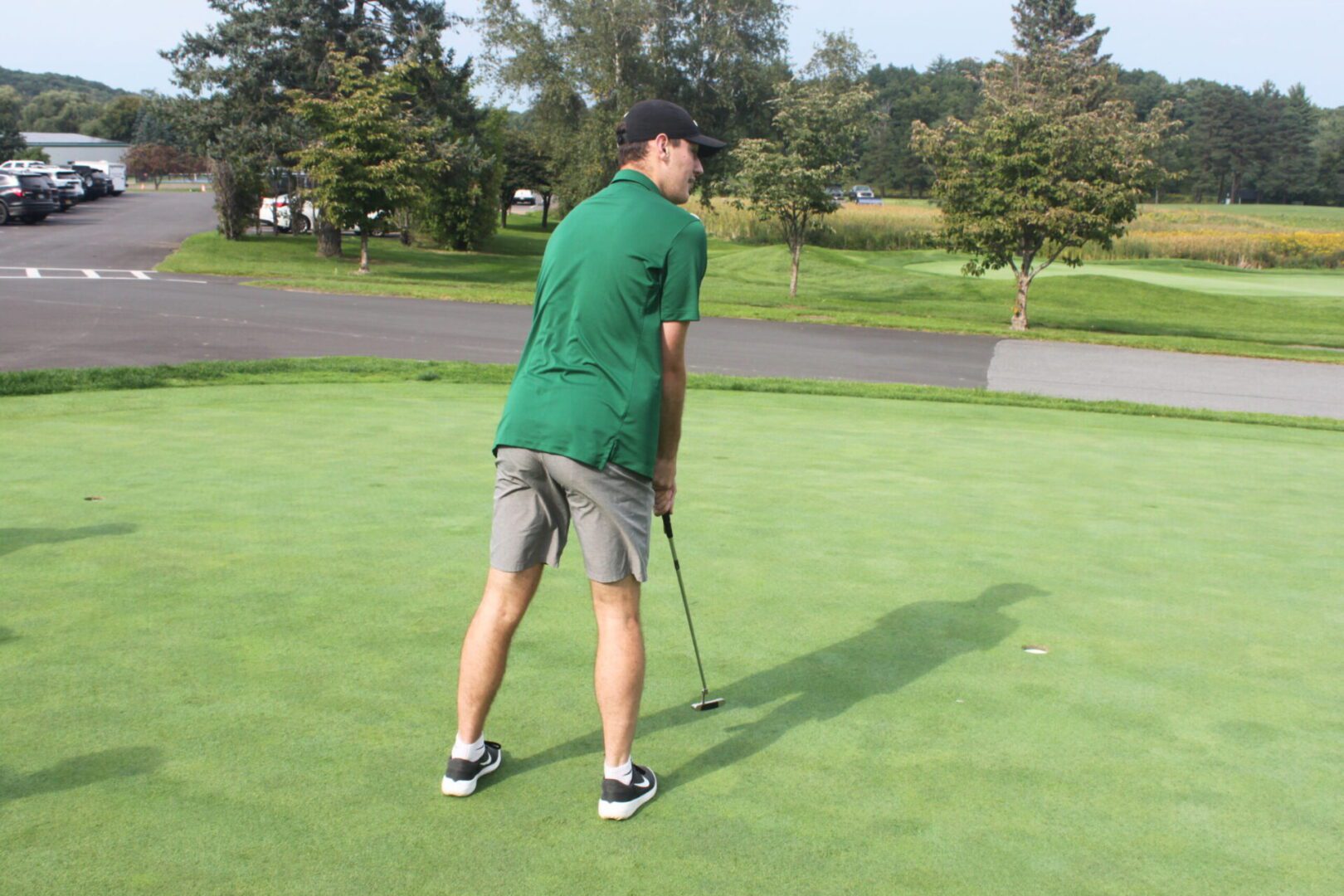 A man in a green shirt is putting a golf ball.