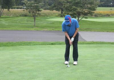 A man in a blue shirt is putting a golf ball on a green.