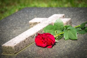 A rose lying on the ground near a cross sign