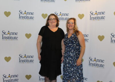 Two women standing in front of a heart banner.