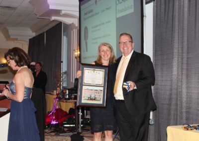 A man and a woman standing next to each other holding a framed award.