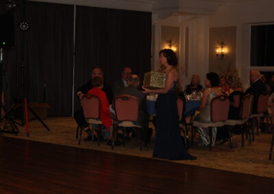 A woman in a dress standing in front of a room full of people.